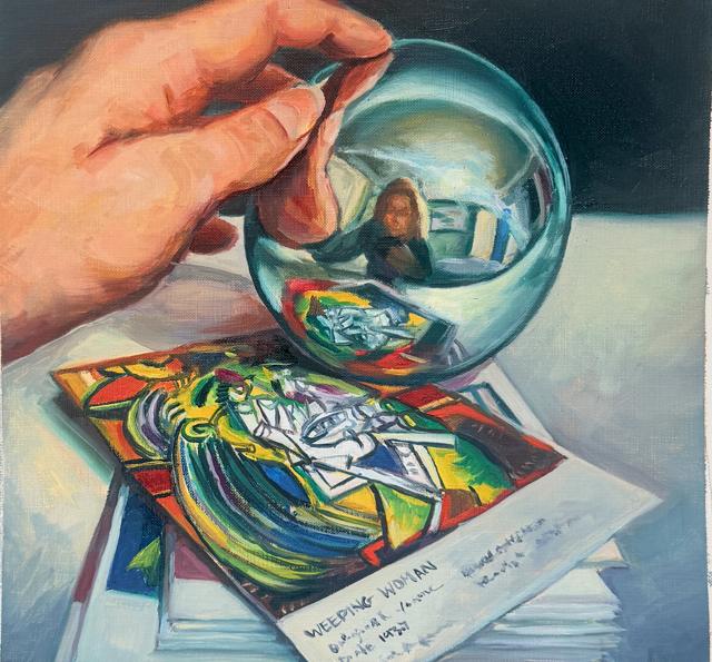 A hand holding a mirrored glass sphere reflecting the artist, resting on a Picasso Weeping Woman print