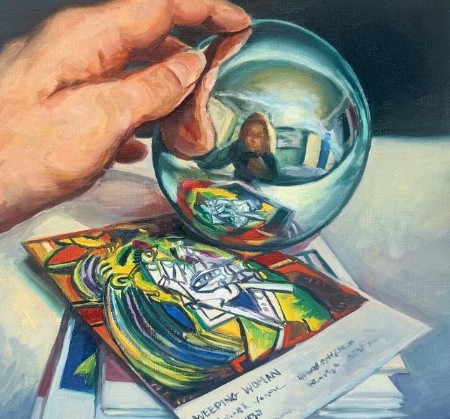 A hand holding a mirrored glass sphere reflecting the artist, resting on a Picasso Weeping Woman print